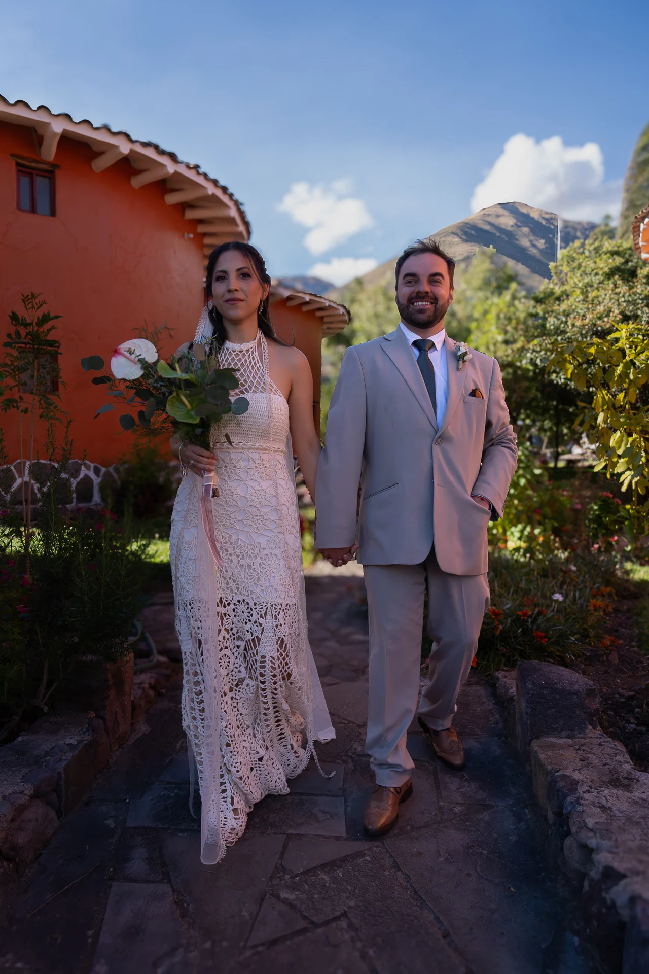 Los recién casados caminan de la mano entre jardines y montañas